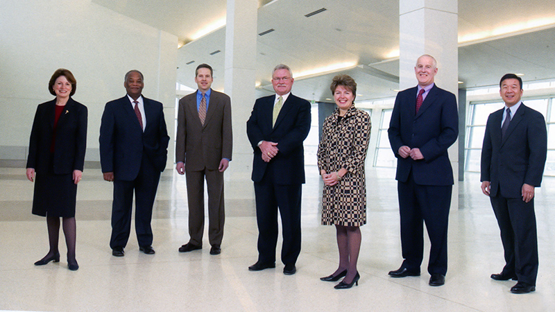 Port of Seattle Executive Leadership standing together in a lobby. Gina Marie Lindsey, third from the right, wears a black and tan patterned dress.