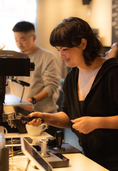 A person practicing espresso preparation at Coffee Tab while another person works in the background.