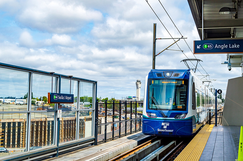 A Sound Transit light rail train arriving at an outdoor station platform, with signage for SeaTac/Airport and Angle Lake visible.