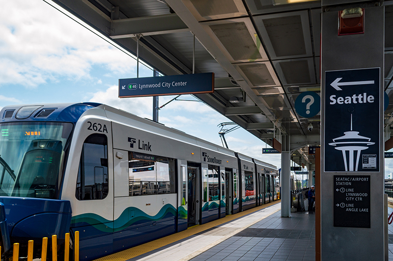 A Link light rail train is stopped at a station platform with signs pointing toward Seattle and Lynnwood City Center.