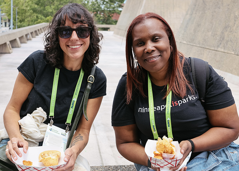 Two people seated outdoors holding trays of Ezell’s Chicken at a tour stop.