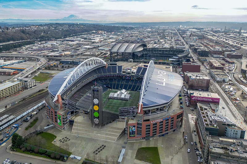 Aerial view of Lumen Field surrounded by city streets, rail lines, and nearby stadium structures.