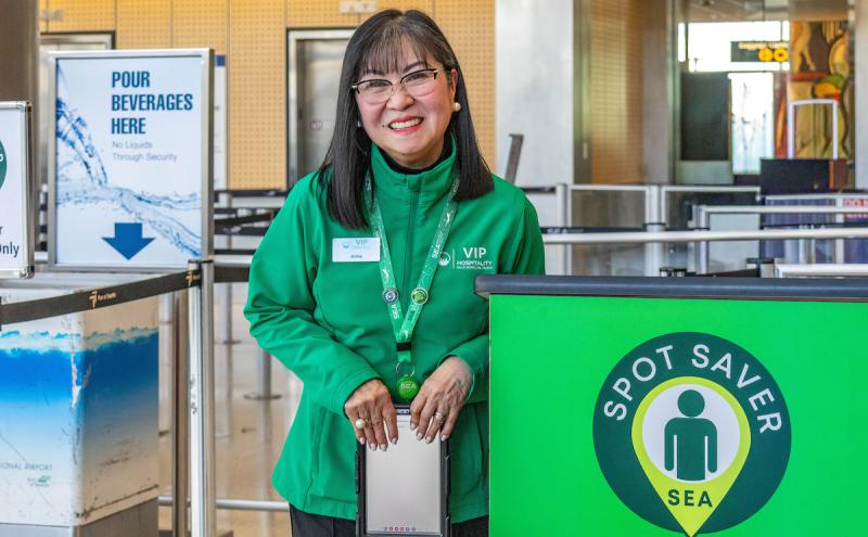 SEA Spot Saver employee is wearing a green jacket and smiling by the Spot Saver podium