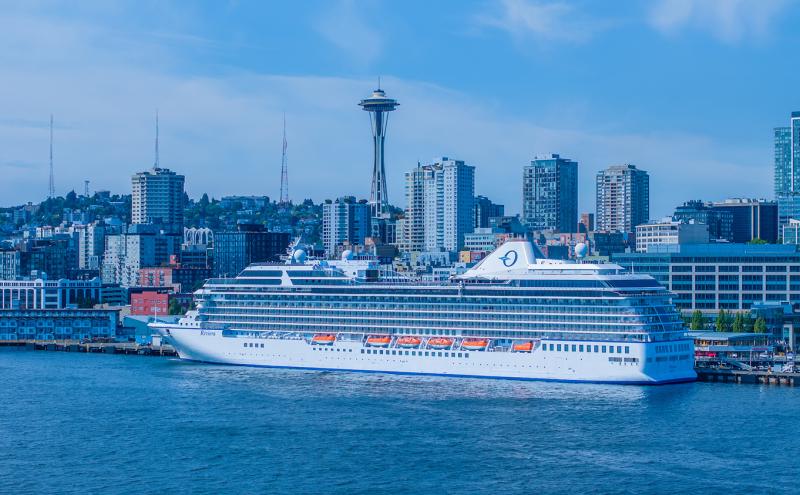 The cruise ship Oceania Riviera departing from Pier 66 in Seattle with the city skyline and the Space Needle in the background.