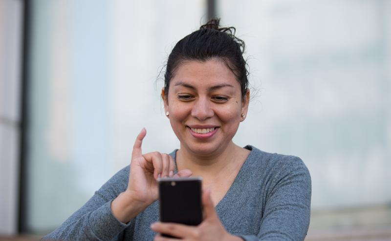 An individual outdoors holding a smartphone and looking at the screen, illustrating the use of a mobile device as part of Mobile VRI services.