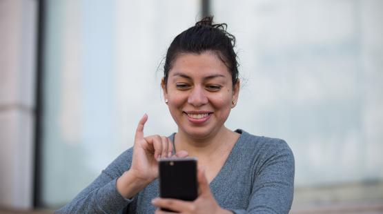 An individual outdoors holding a smartphone and looking at the screen, illustrating the use of a mobile device as part of Mobile VRI services.