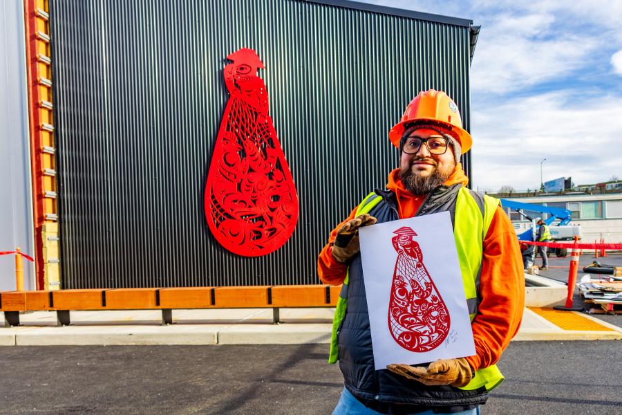 Ty taking a photo holding his Beach Seining draft in front of his finished Beach Seining sculpture at Fishermen's Terminal
