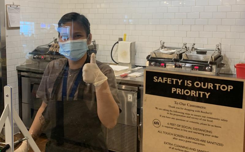 Dining employee wearing a face covering behind plexi-glass at SEA gives a thumbs up, May 2020 