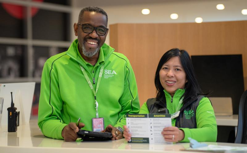 Two pathfinders airport employees at information booth smiling.