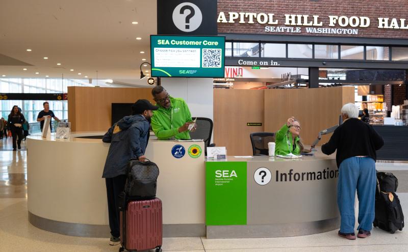Two pathfinders seated at an information booth, both assisting passengers.