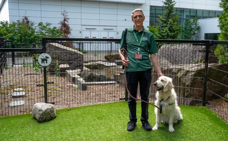 Pet and owner at the relief area with green grass and black fencing outside the terminal on a sunny day
