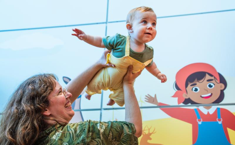 Infant is held up by parent and holds out their arms like they are flying.