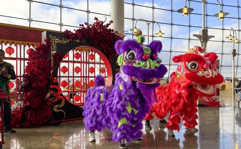 2025 Lunar New Year display in front of the window wall at central terminal. Includes two traditional dancers in red and purple costumes.