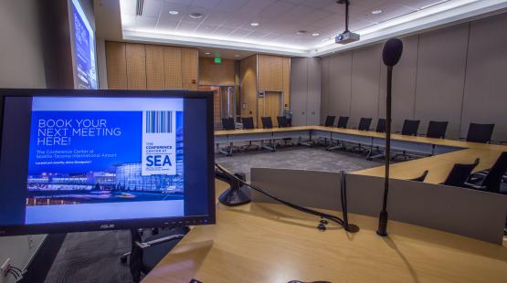 View from the podium located inside the Amsterdam Conference room featuring a hollow square room set with the projector and dropdown screen